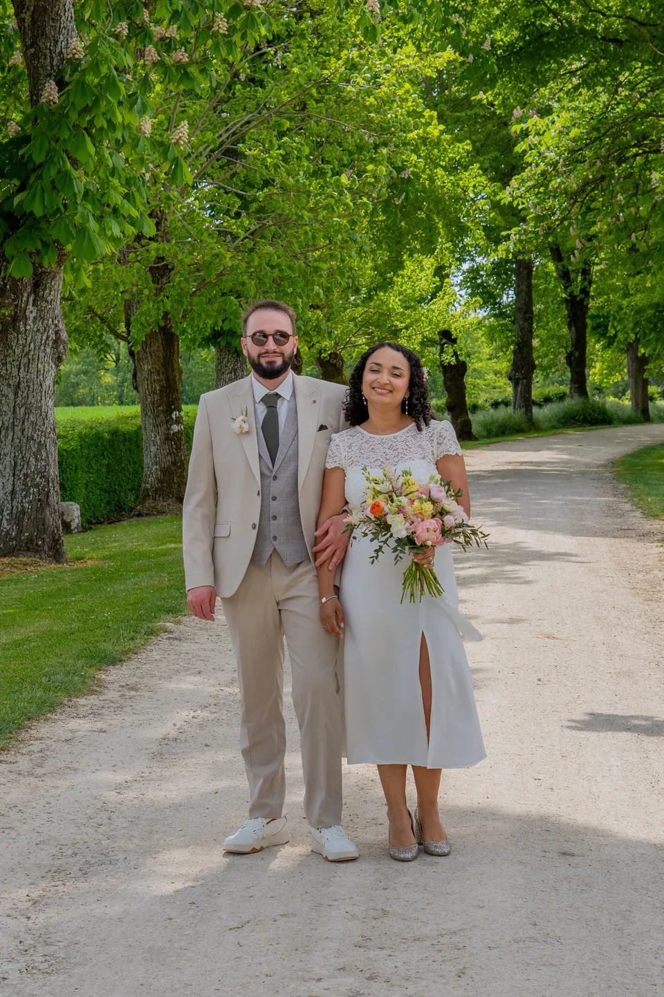 Les mariés posent sur le chemin bordé d'arbres, bouquet à la main